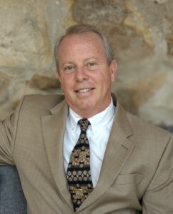Man in beige suit with patterned tie.