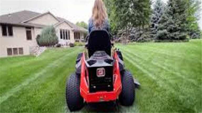 Person mowing lawn with red riding mower.